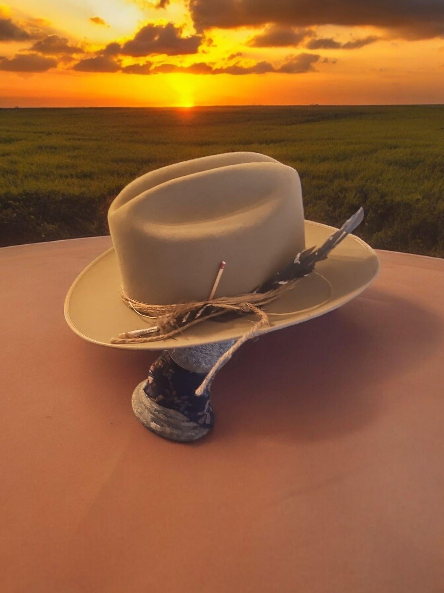 Spirit Warrior Provisions beige 6X wool felt Western hat with a decorative cord hatband at sunset in a field.