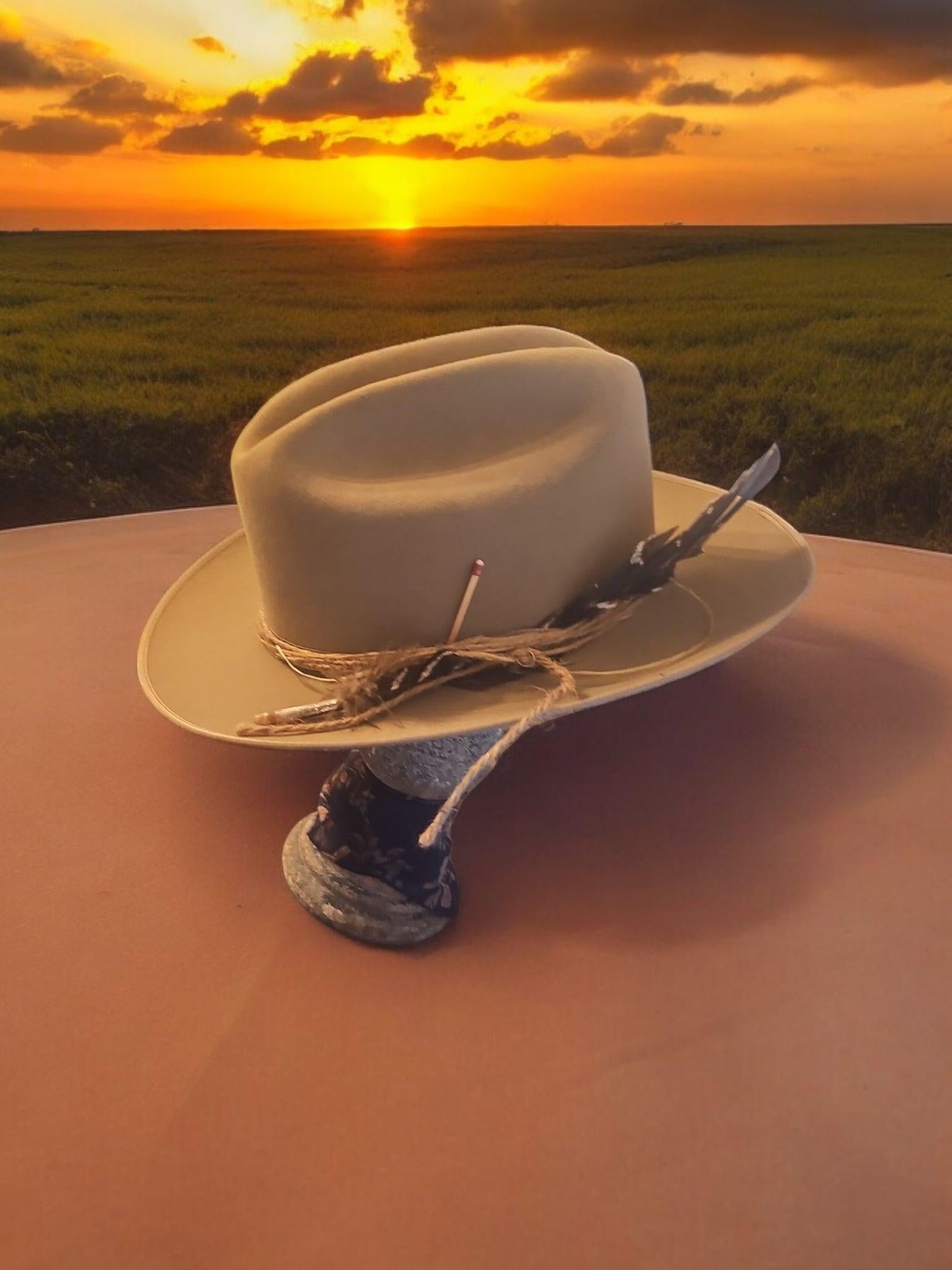Spirit Warrior Provisions beige 6X wool felt Western hat with a decorative cord hatband at sunset in a field.