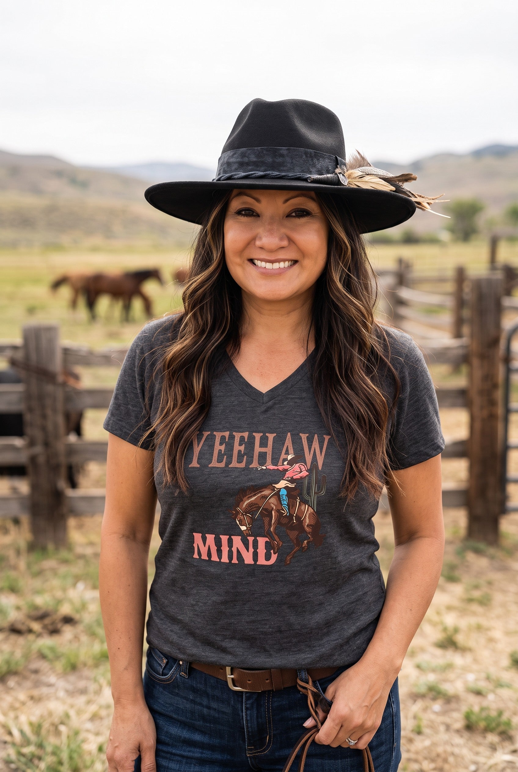 Woman wearing a Spirit Warrior Provisions black felt pinch front hat with feather detail on a ranch with horses