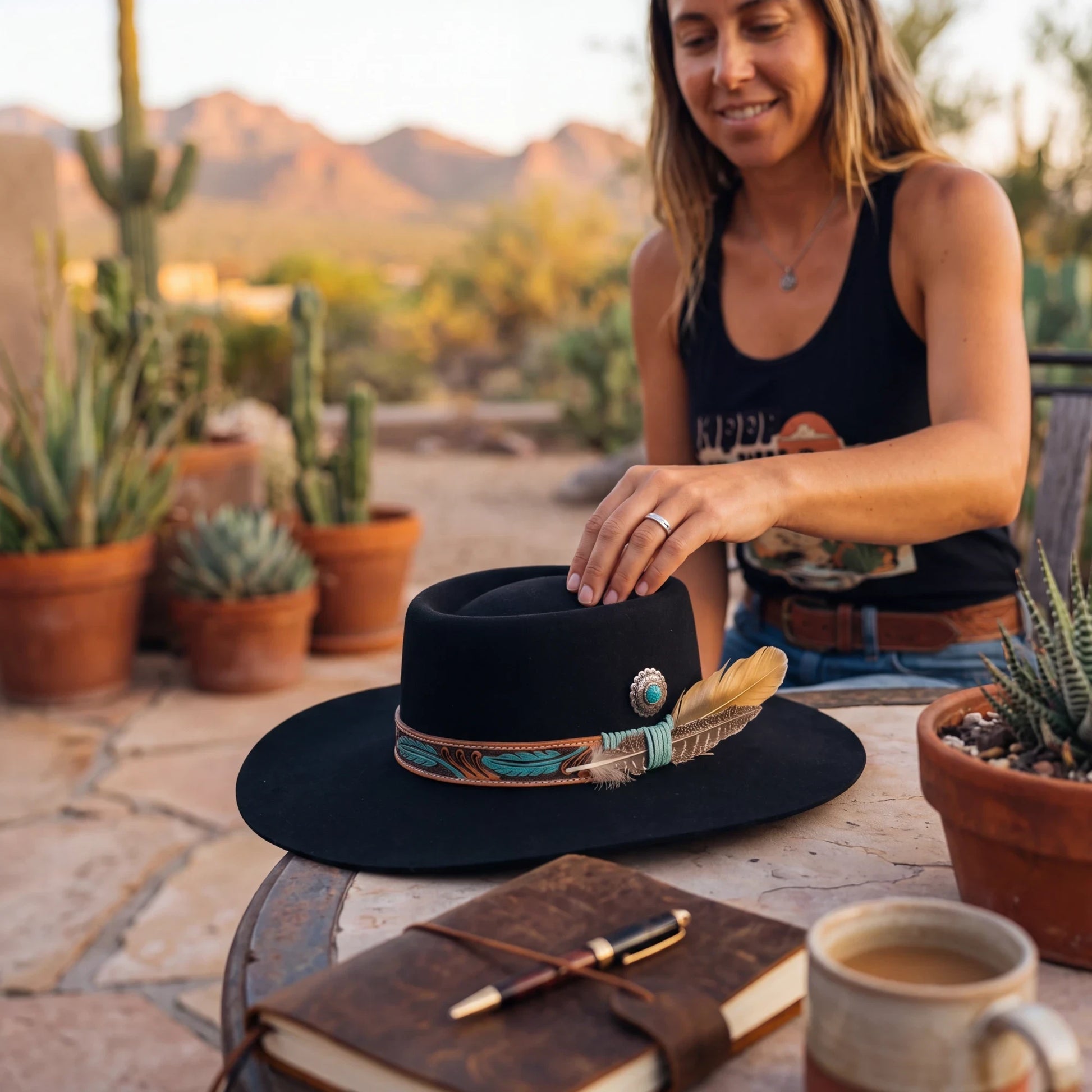 Spirit Warrior Provisions black gambler felt hat with tooled leather band, turquoise concho, and feathers on a patio.