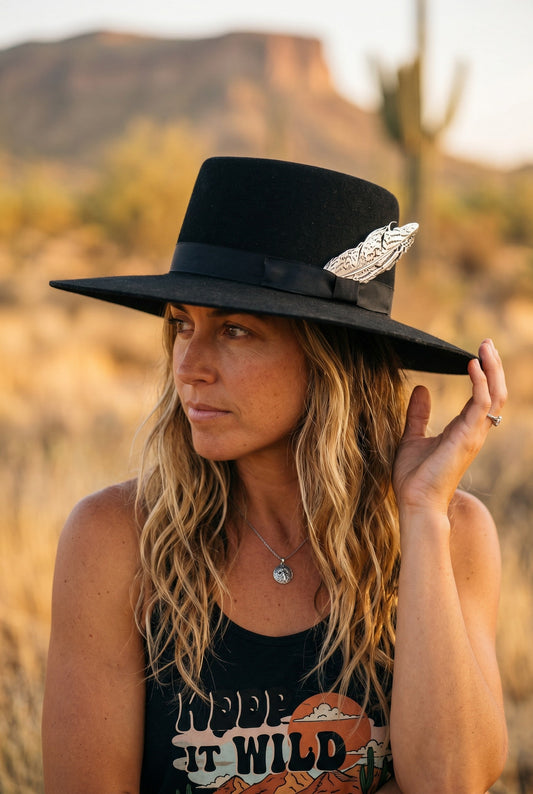Spirit Warrior Provisions black gambler felt hat with a 4-inch brim, silver pheasant tail, and buckle on a woman.