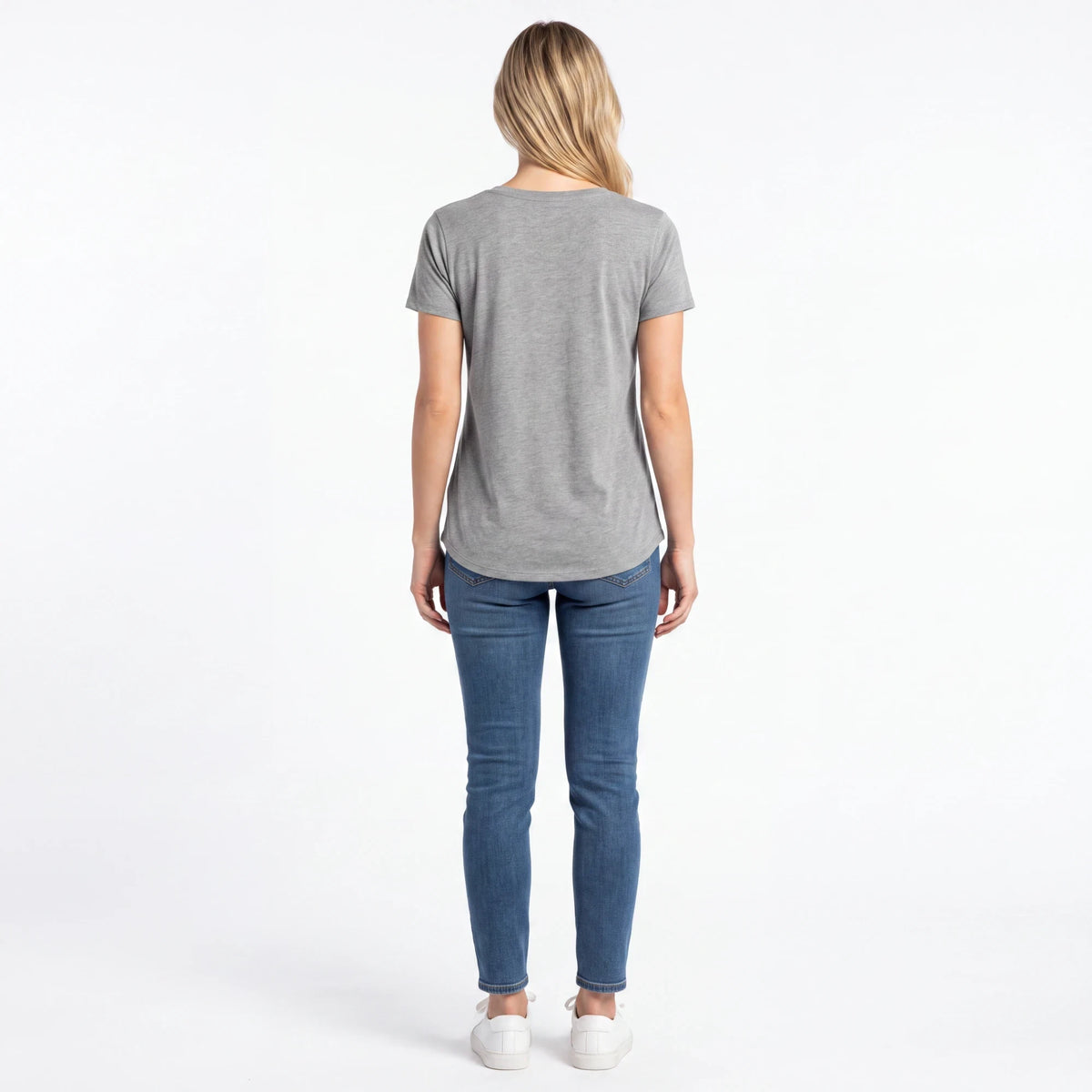 Back view of a woman wearing a Spirit Warrior Provisions grey cotton t-shirt with blue skinny jeans and white sneakers