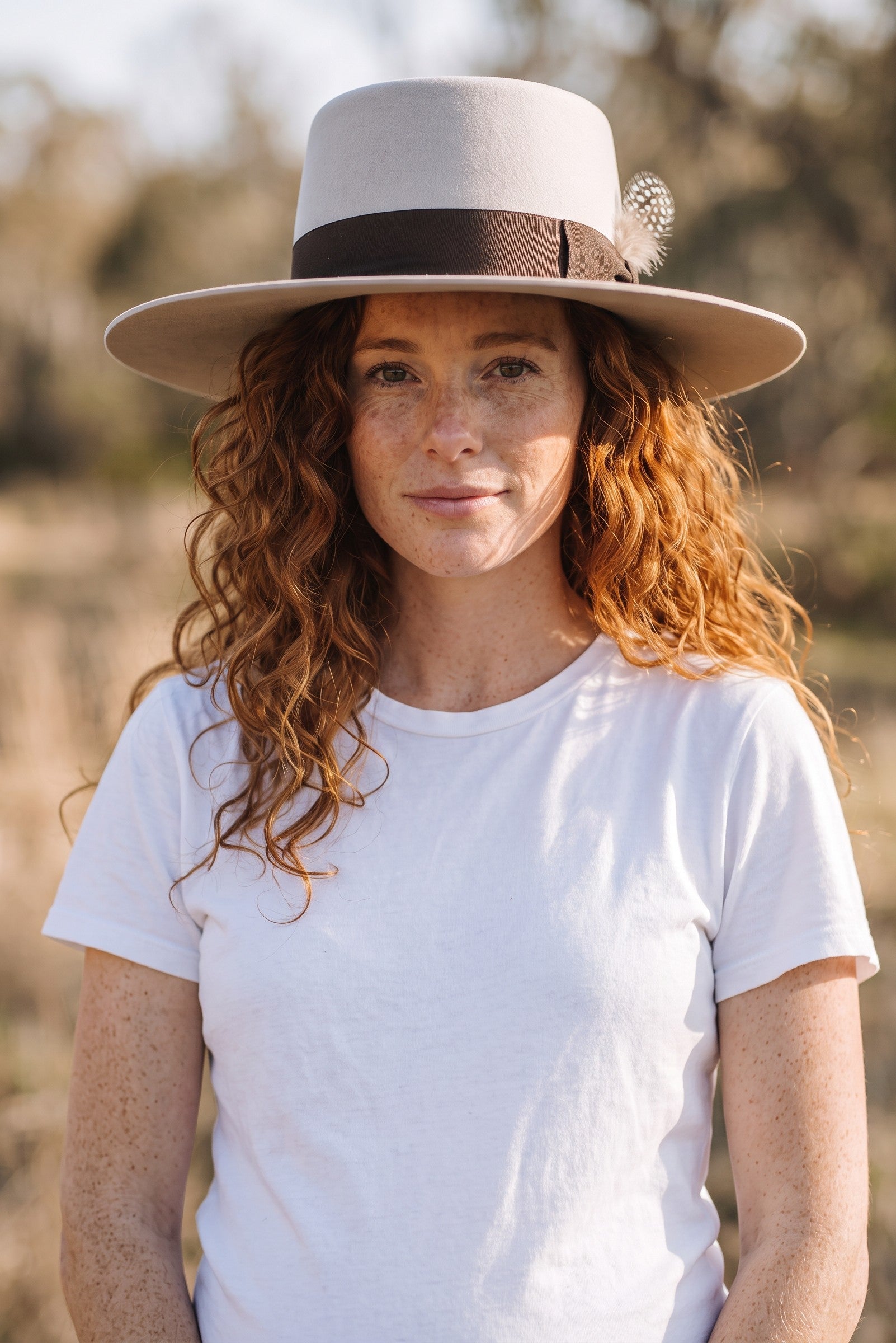Spirit Warrior Provisions sand gambler hat with flat brim and grosgrain ribbon worn by a woman with curly red hair.
